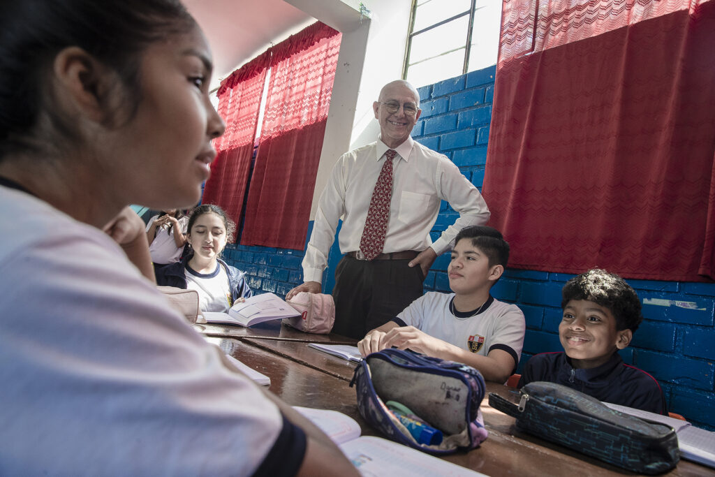 A man stands with students sitting at desks in front of him