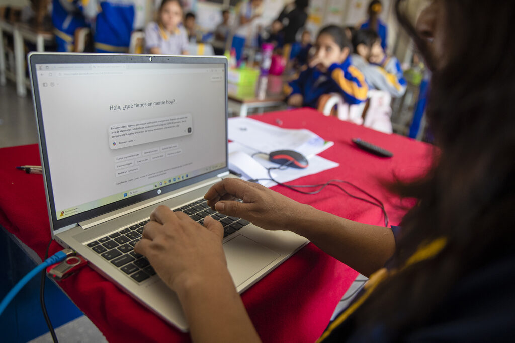 A woman sits at a desk working on a laptop with a Copilot session displayed
